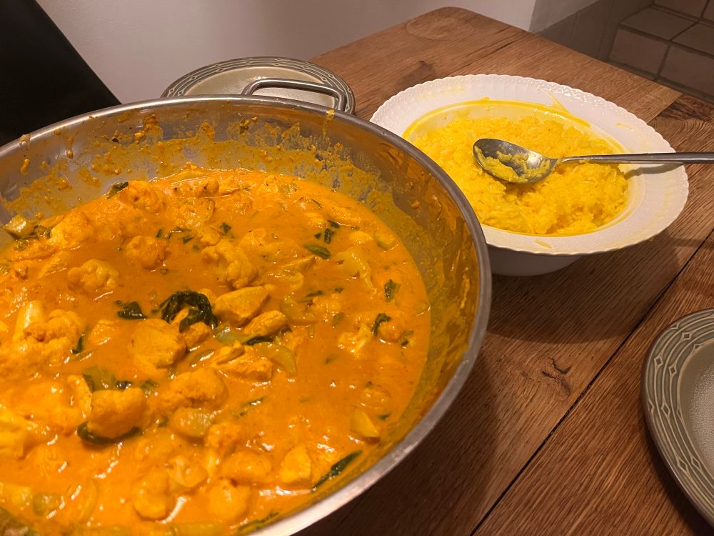 Said dish on a wooden table in a large wok pan and a porcelain dish with yellow saffron rice