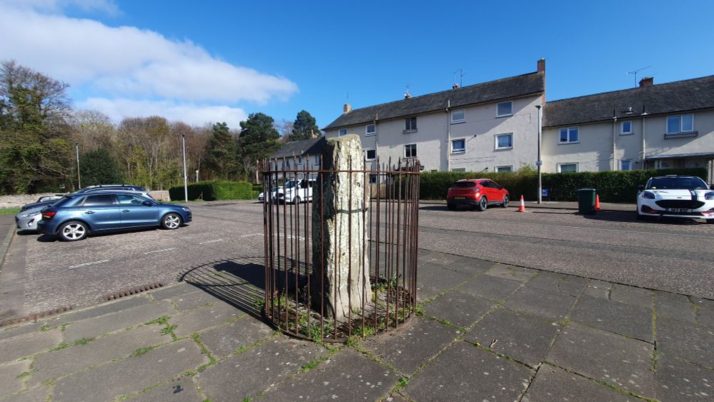 Standing stone in a cage, situated in a car park beside houses. Ravenwood Avenue, Edinburgh.