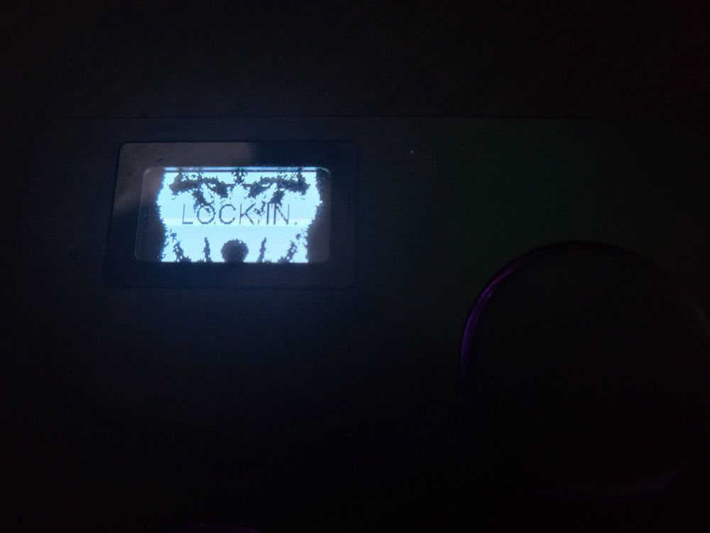A close-up of the screen showing a low resolution black and white image of a focused wolf with text saying "LOCK IN."