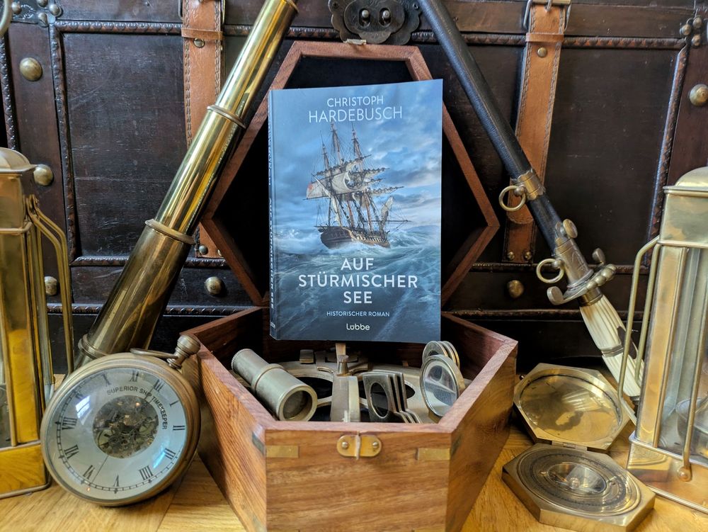 Photo des Romans "Auf Stürmischer See" umgeben von nautischen Paraphernalia wie Kompass und Sextant 