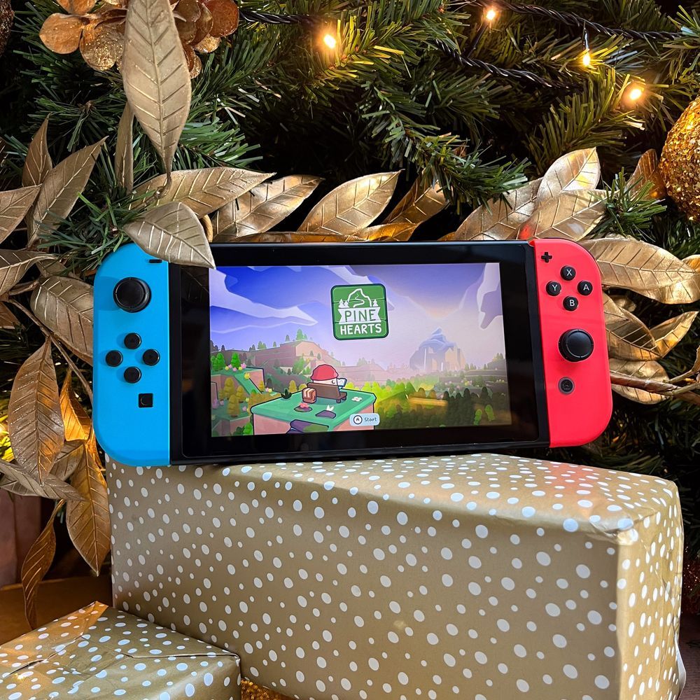 Nintendo Switch console playing Pine Hearts, resting on top of some presents under a decorated Christmas Tree.