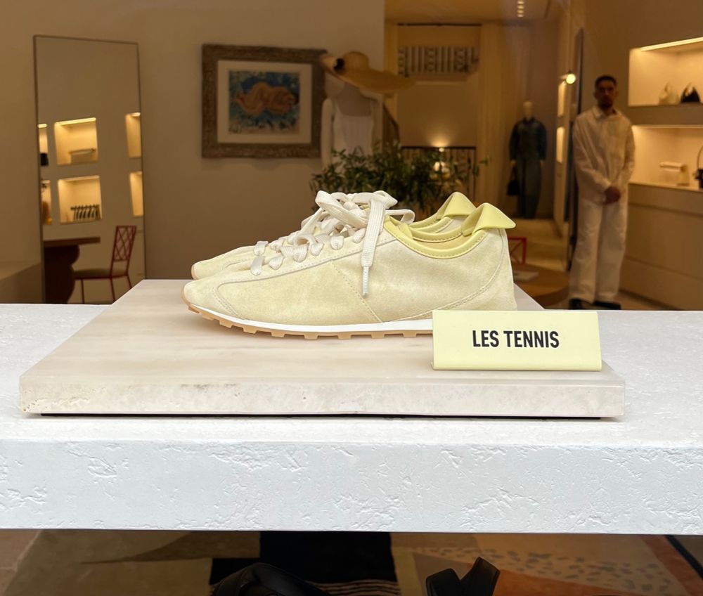 A pair of pale yellow trainers in a shop window with a label reading Les Tennis