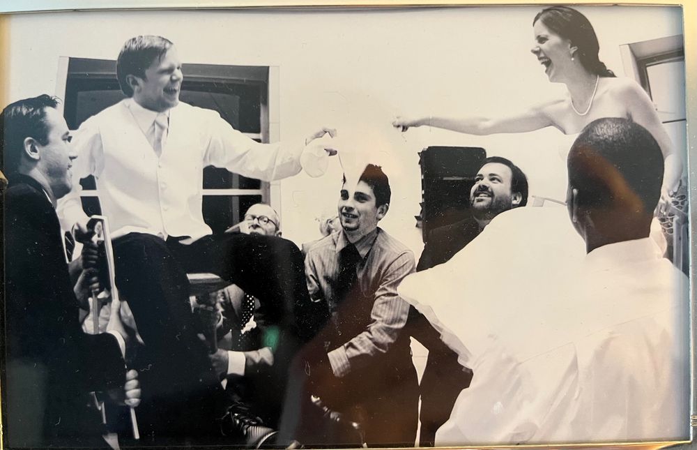 Wedding photo of bride and groom being lifted on chairs during the hora 