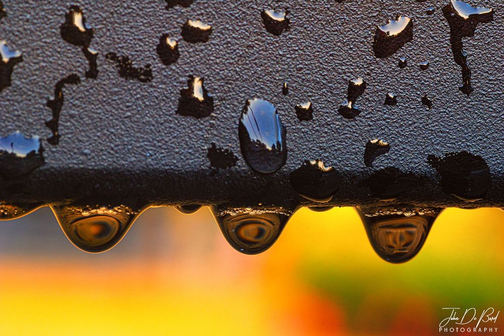 Raindrops on a steel railing against the colors of sunset. 