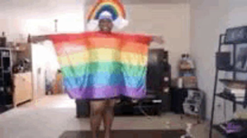 a person is standing in a living room wearing a rainbow poncho and a rainbow hat .