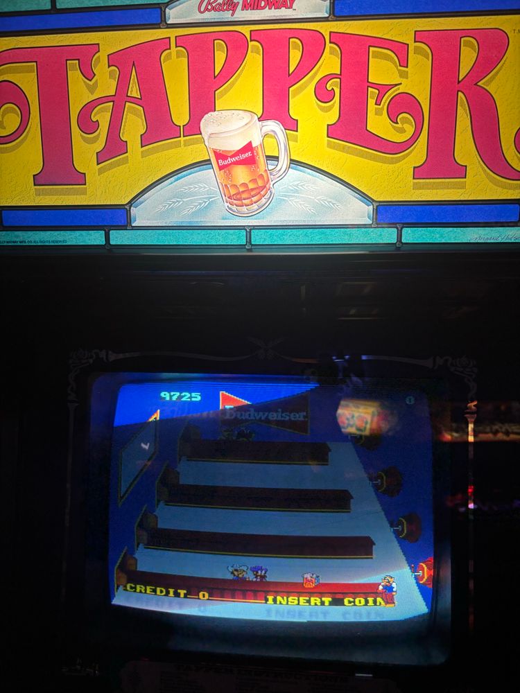 The marquee of a video game cabinet for the game Tapper by Bally Midway. It is a game about to bring Budweiser beer to patrons of different venues