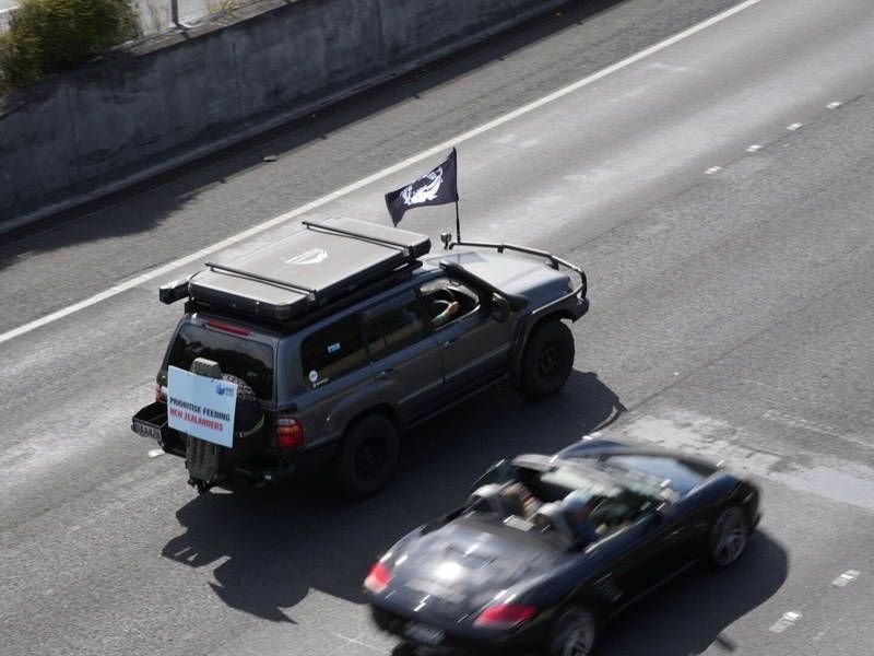 Protest vehicle driving with a poster saying "Prioritise feeding New Zealanders." 
