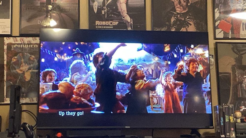 Shot of a television displaying a scene from the beginning of Fellowship of the Ring. The scene depicts hobbit children being entertained by Gandalf at Bilbo’s birthday party.  