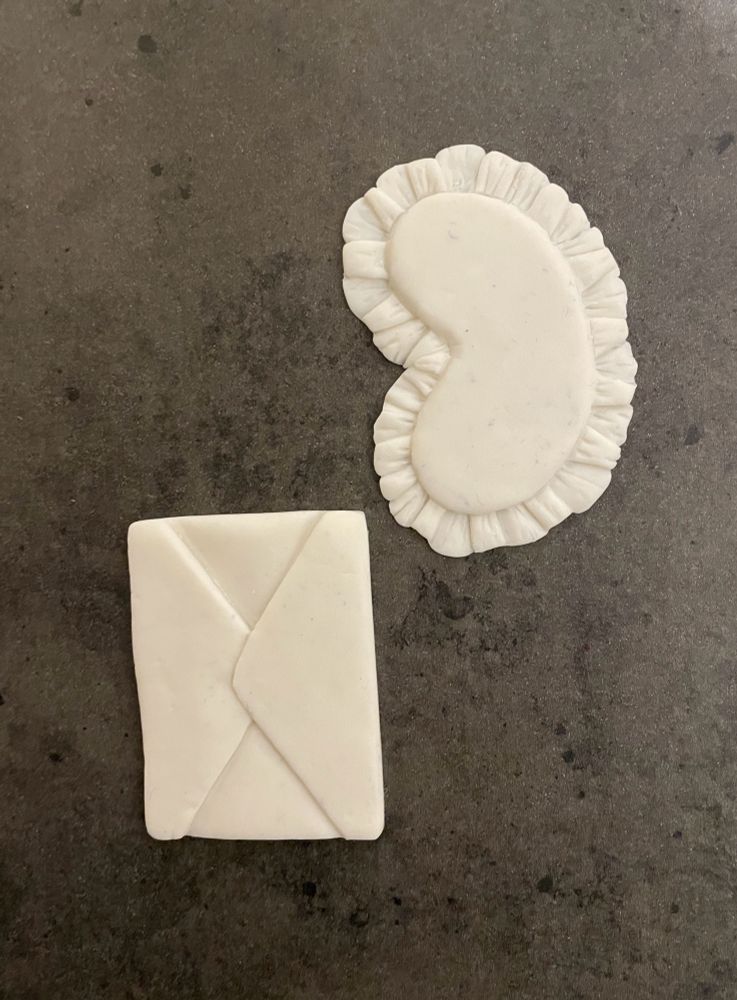 Two DIY Taylor ornaments. One is an envelope and one is a sleep mask. Both are white (with little specks of dust, wooopsie) and blank for now