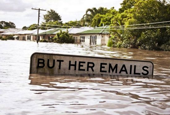 A flooded residential street somewhere in America. Half of a street sign peeks above the waters. It reads, "But her emails."