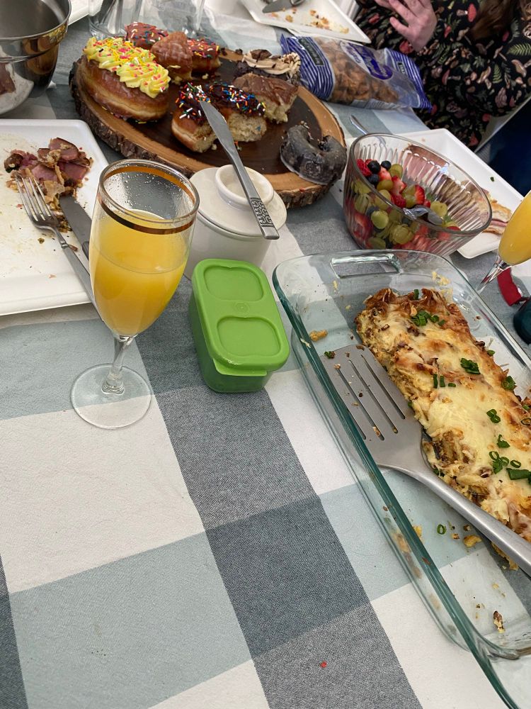 A gingham table cloths with mimosas, plates of food, donuts, and a cheesy casserole. 