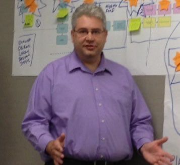 large male-appearing person in purple dress shirt who has a visible paunch.