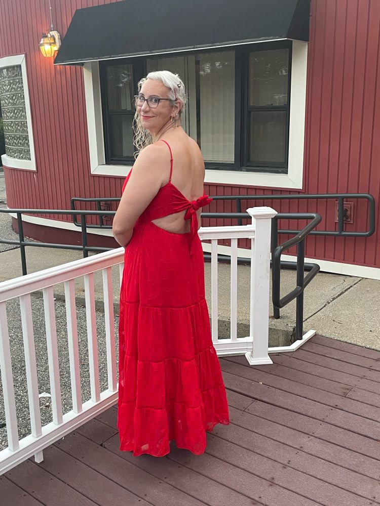 Same gal as before, same red dress. She’s turned so that she sees the camera but her back is turned towards the camera. There is a red ribbon tied around the back of the dress and the rest of the back is cut out to the waist.