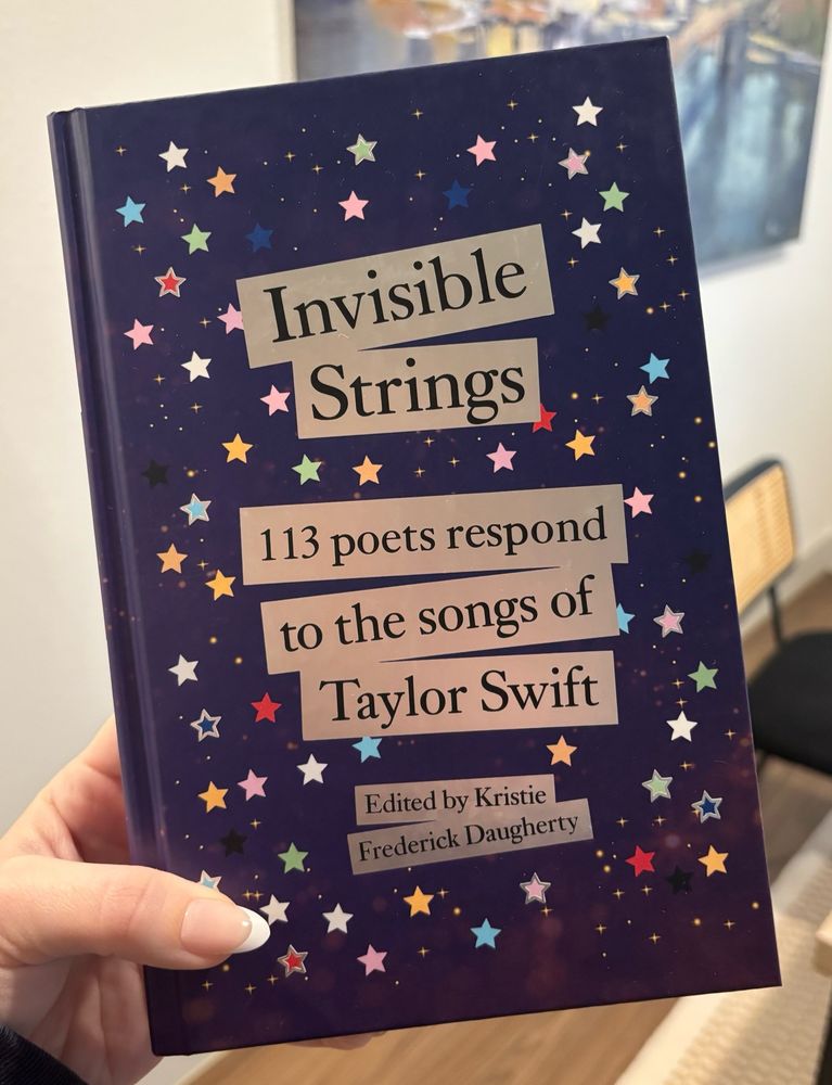 A picture of a hand holding the book “Invisible Strings: 113 poets respond to the songs of taylor swift” by Kristie Frederick Daugherty