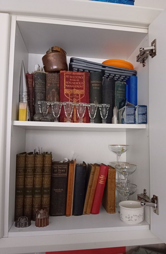 A picture of a collection of antique cook books from the early 1800s to 1920 along with antique Ice cream moulds and Victorian ice cream penny lick Glasses