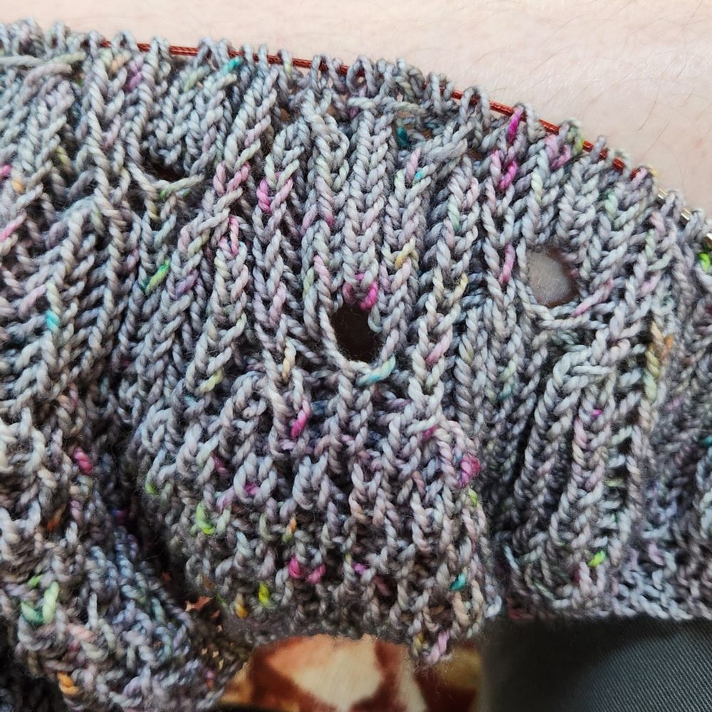 Close up of brioche lace shawl in silvery gray with multi-colored spots. 