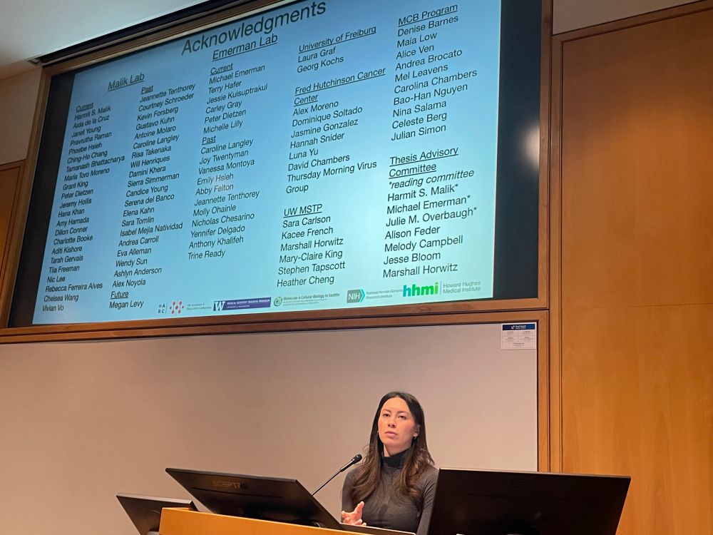 Person in front of a podium answering questions from the audience.  A slide of many acknowledgments is on the screen behind her.