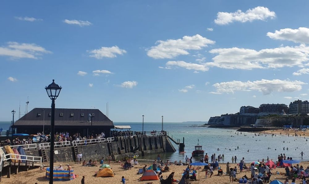 Beach with lots of people.  Calm blue sea and blue sky with fluffy white clouds.  Fuck off Farage you racist piece of shit.