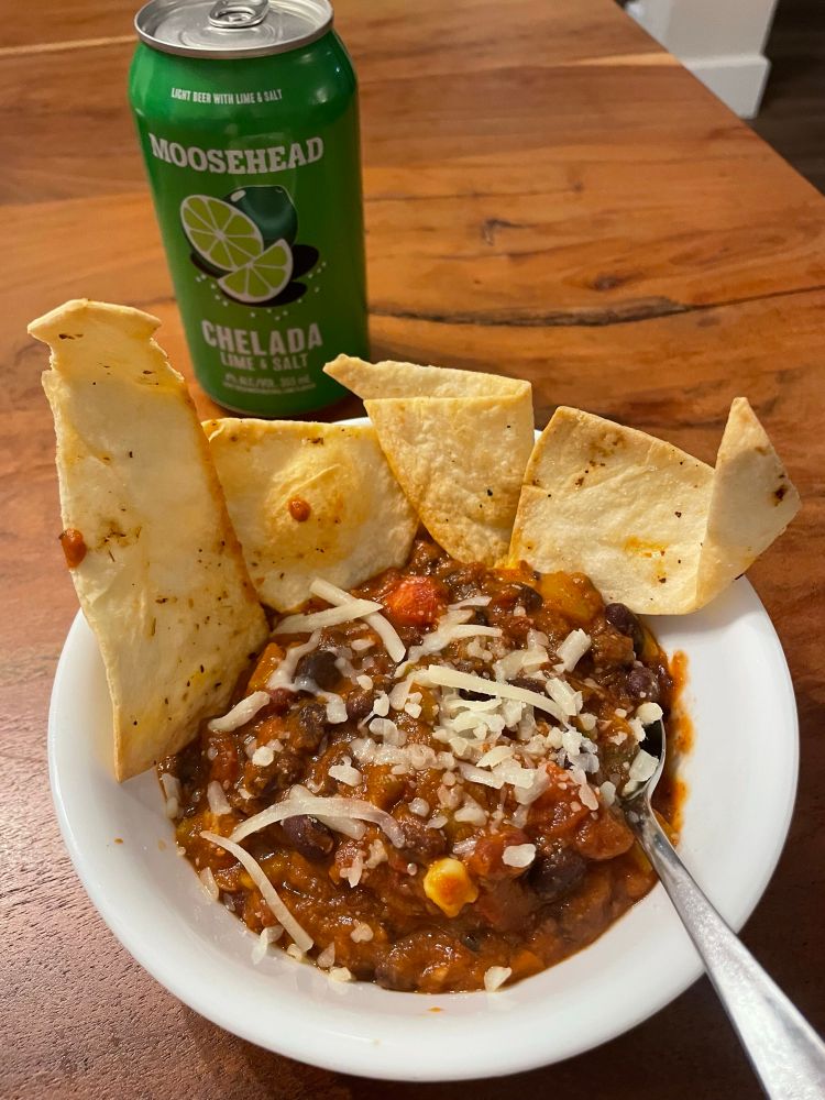 Bowl of veggie chili topped with shredded cheese with air fried tortilla chips on the side. 