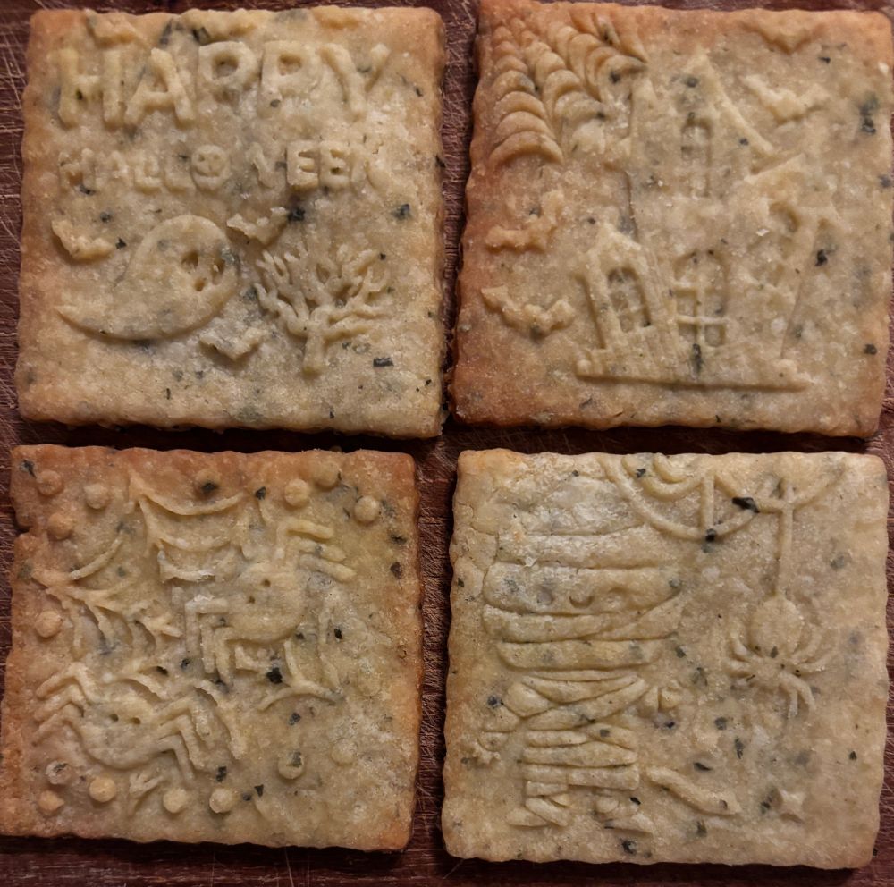 4 cookies laid out next to each other, each has a Halloween design stamped onto it: a ghost, a witches hut, a spider’s net, and a mummy