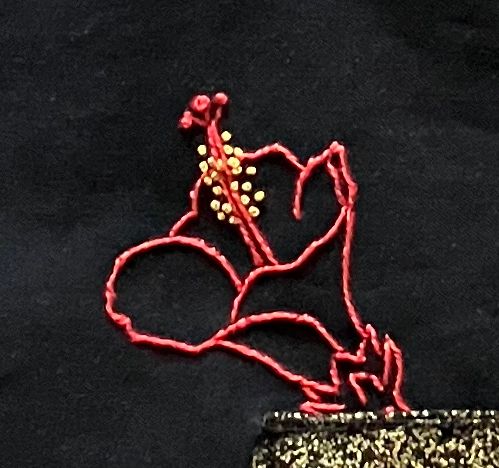An embroidered red hibiscus flower on black fabric