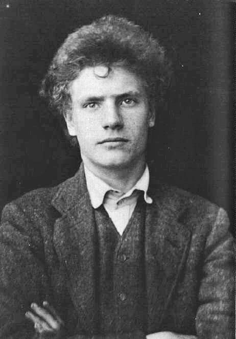 Nesta fotografía en branco e negro vemos a Austin Osman Spare, un recoñecido artista e ocultista británico do século XX. Spare aparece en posición frontal, mirando directamente á cámara cunha expresión seria e penetrante que reflicte intensidade e introspección. O seu rostro é novo, de trazos marcados, cun nariz prominente, beizos lixeiramente pechados e ollos penetrantes que transmiten unha sensación de profundidade e misterio.

O seu cabelo é rizado e voluminoso, un pouco desordenado, o que contribúe á súa aparencia distintiva e artística. Viste unha camisa con colo, cuberta por un xersei e unha chaqueta, reflectindo o estilo masculino clásico da época. Os seus brazos están cruzados sobre o peito, un xesto que pode suxerir determinación, confianza ou unha actitude introspectiva.

A iluminación resalta os seus trazos faciais, mentres que o fondo é escuro, centrando a atención exclusivamente na figura de Spare. Esta foto captura a esencia do artista, evocando unha aura de misterio e introspección, acorde coa súa personalidade como creador de imaxes esotéricas e explorador do inconsciente.