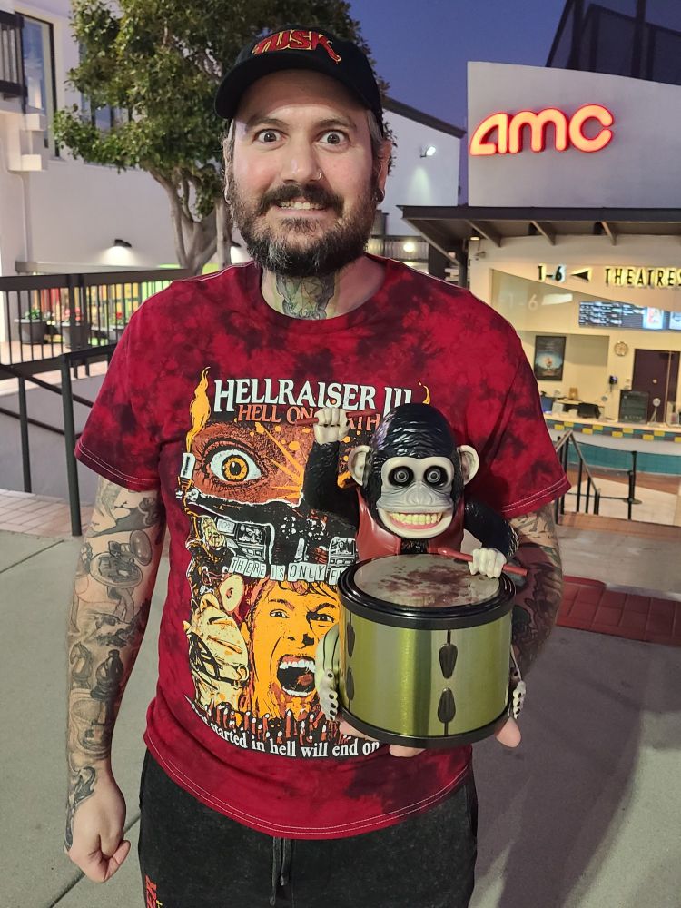 Me doing my best impression of The Monkey while holding an AMC popcorn bucket modeled after NEON's The Monkey