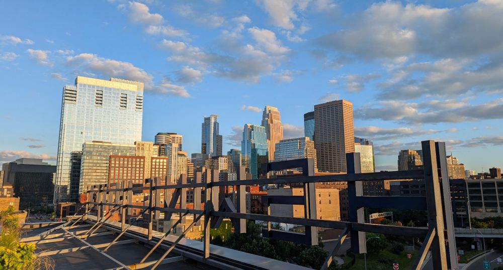 A photo of Minneapolis's skyline at sunset. Viewed from a rooftop with the letters HEWING HOTEL in front of the skyline. 