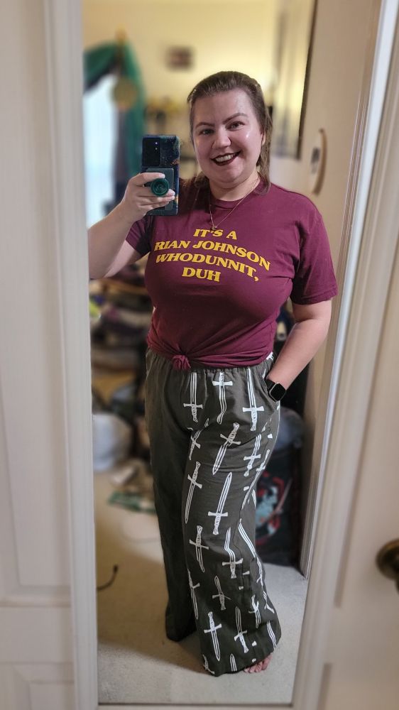 picture of me in a red t-shirt that reads "it's a rian johnson whodunnit, duh" and olive pants with white knives on one leg