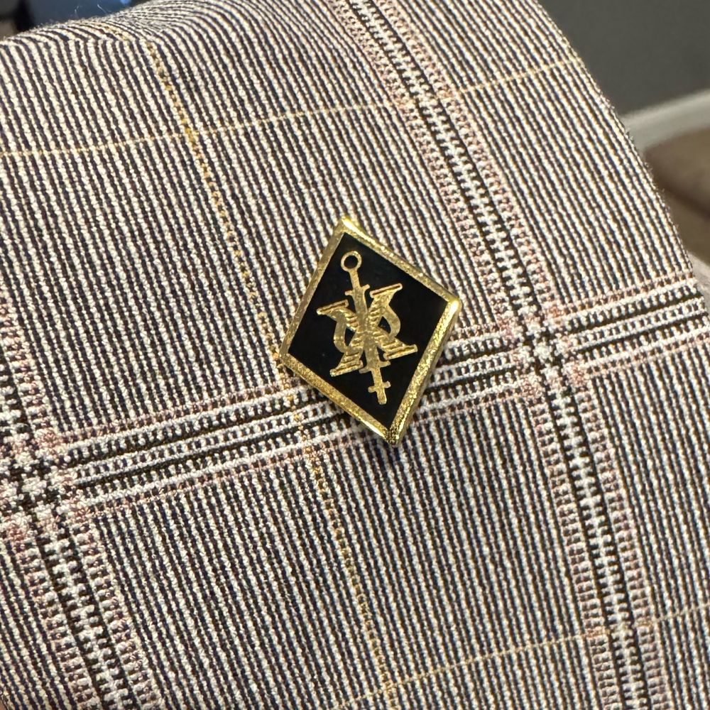 A close-up photo of the Psi Chi membership pin affixed to the lapel of a plaid blazer.