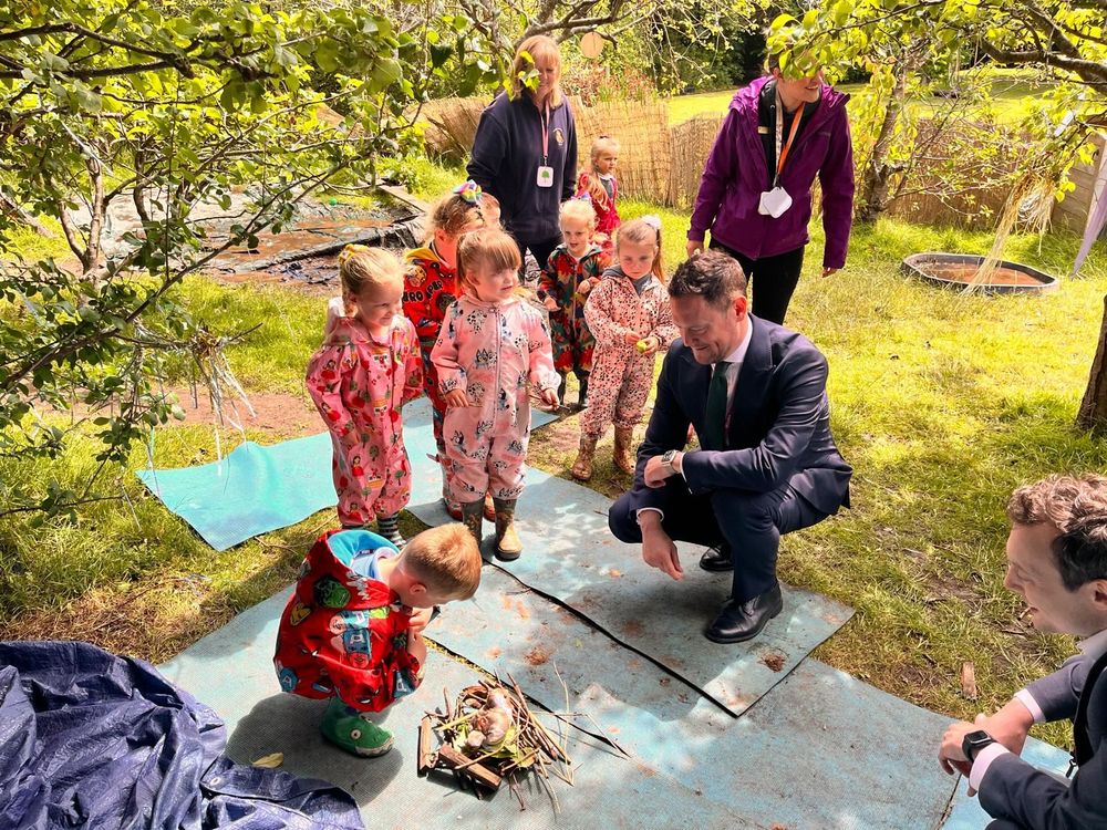 A group of children in rain wear stand under trees looking at a birds' nest with Stephen Morgan and Matthew Patrick observing