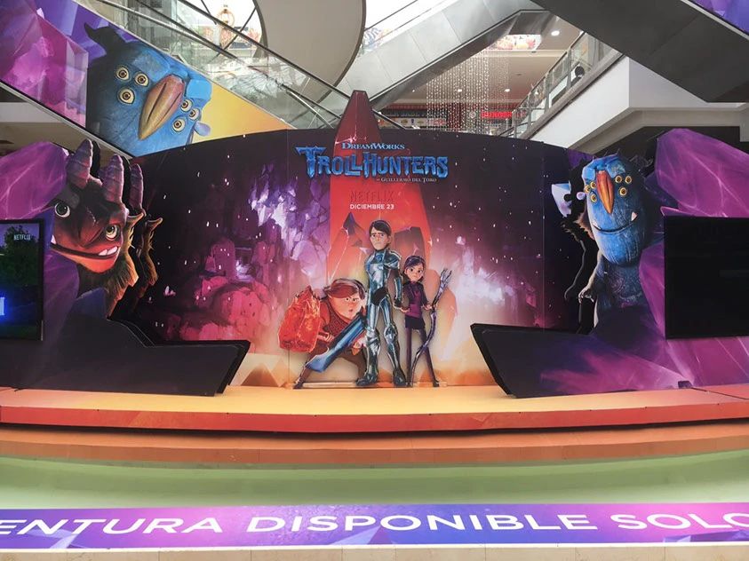 Photograph showing the main point of the Trollhunters display by Daniel Ochoa Vanegas. The center piece shows the kids with weapons and Jim in Daylight standing before the Heartstone with Trollmarket scenery around them. On the left by a TV screen and crystals is AAARRRGGHH whereas on the right is Blinky with the same crystals and TV. There's also an ominous Blinky peering over the top left from the stairs.
