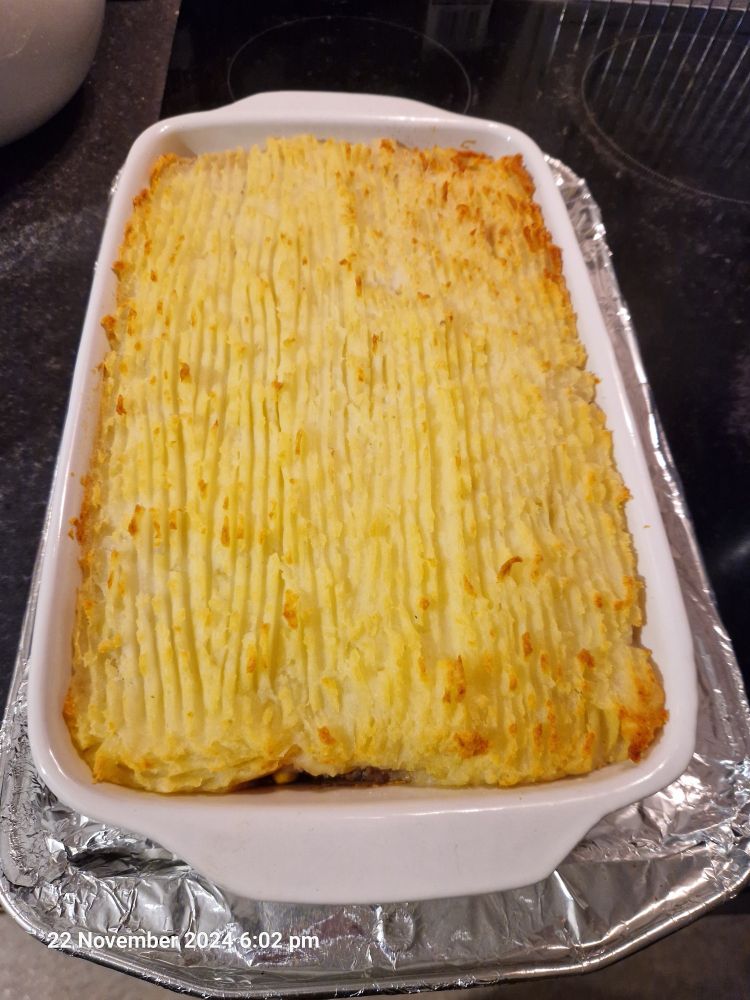 Photograph of an oven proof dish with a layer of golden mashed potato visible - cottage pie, a UK food item made of minced meat and veg cooked in a stock, topped with a layer of mashed potato and then baked.