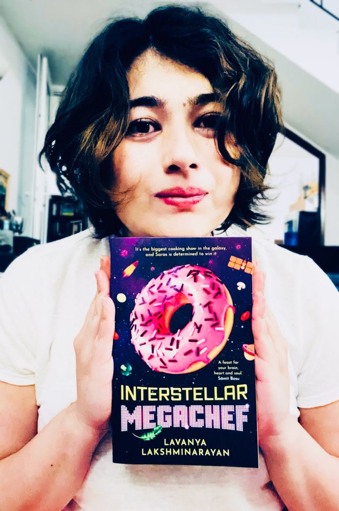 A close up of me, wearing a white t-shirt, holding a copy of my new book, INTERSTELLAR MEGACHEF.