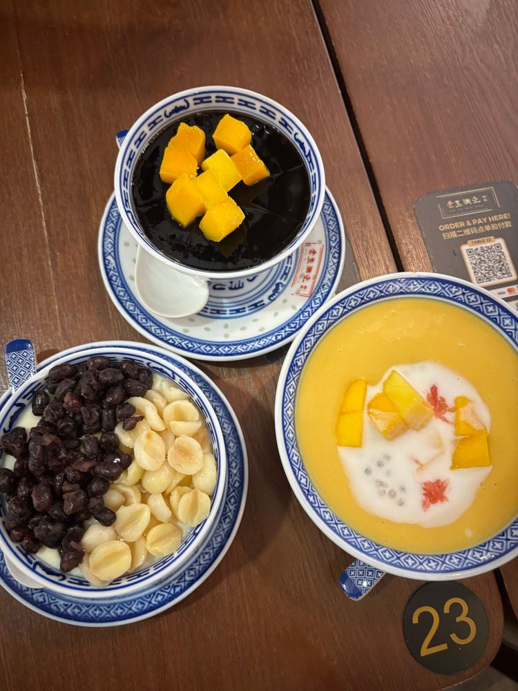 Desserts! Three bowls of dessert—one is a custard with red soya beans and lotus seeds, the other is jelly with mango cubes, and the third is a mango pudding with sago and mango chunks.