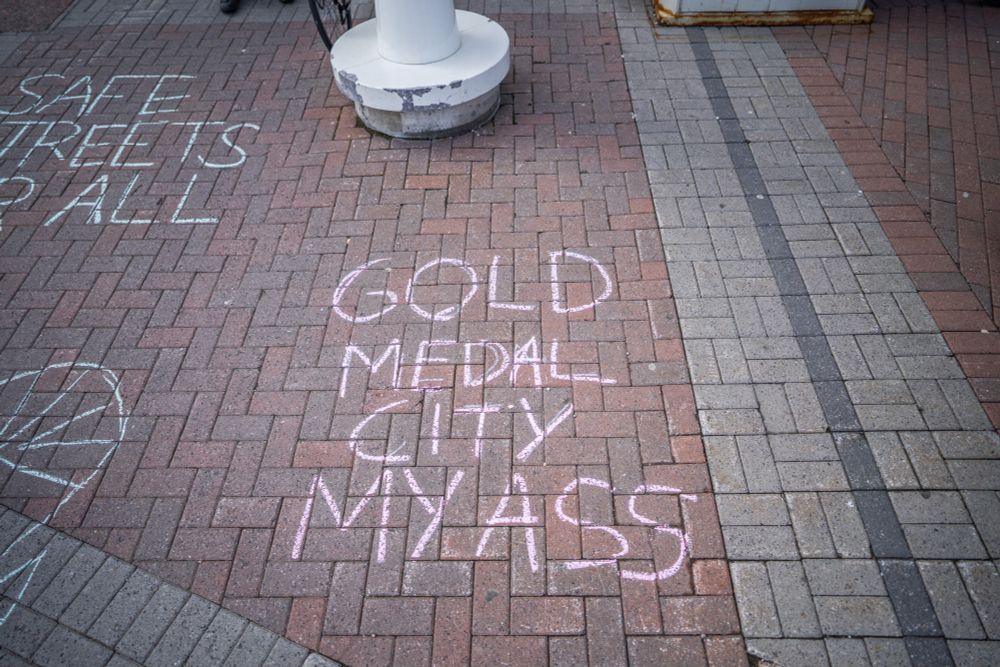 Gold Medal City My Ass is written in chaulk on brown paver stones