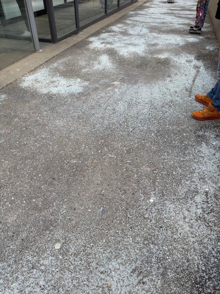 Blue salt covers pavement and the feet of a person in brown boots are visible 