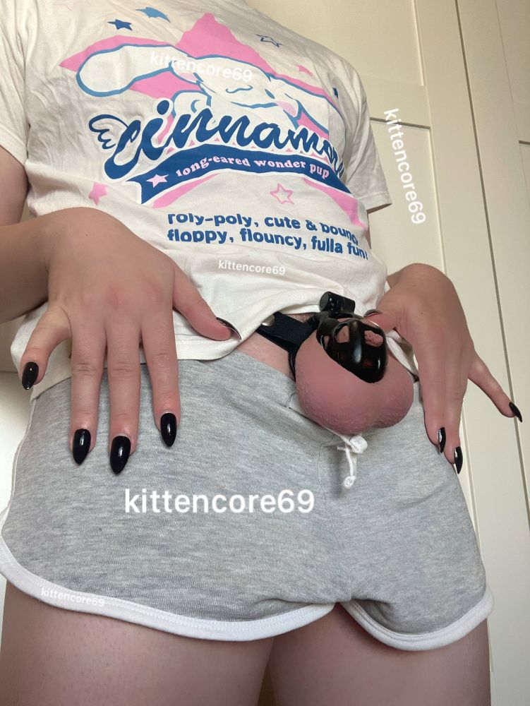 Kat wearing a white top, shorts and a a cage with dark long nails on their waist
