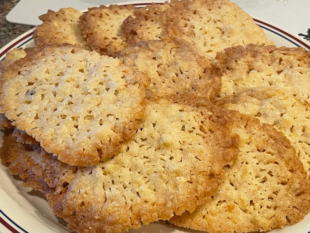 photo of potato chip cookies on a plate with light brown middles and darker edges, the centers are lace style 