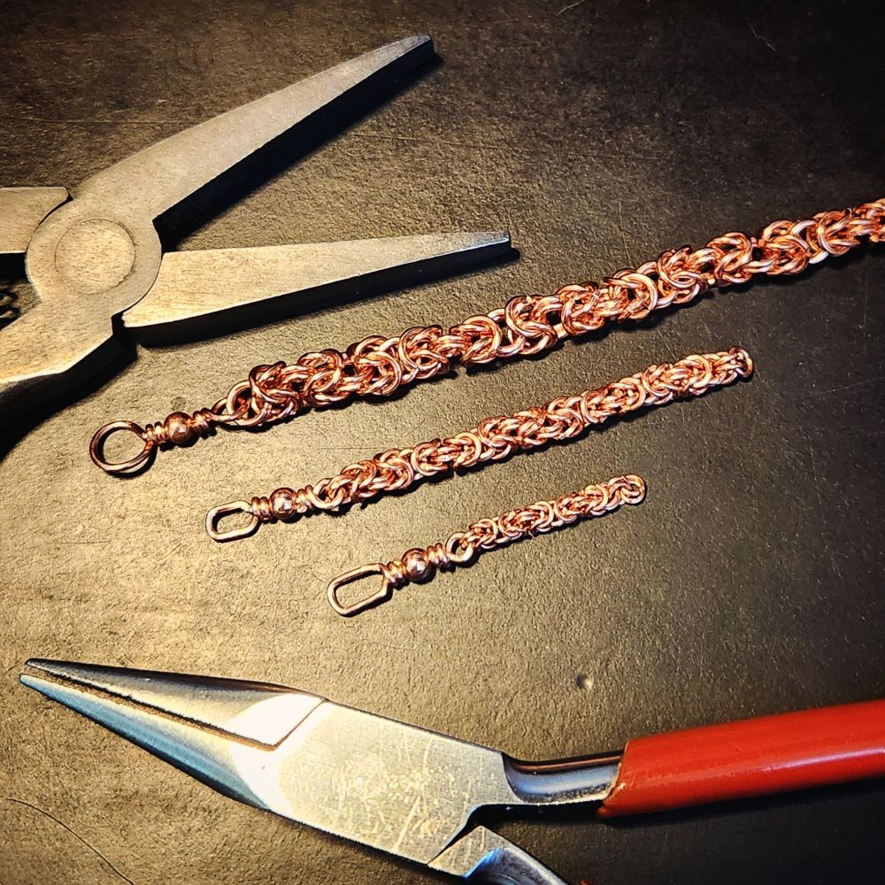short pieces of copper chain in three sizes, medium, small, and super small, on a black work surface, with two pairs of small pliers