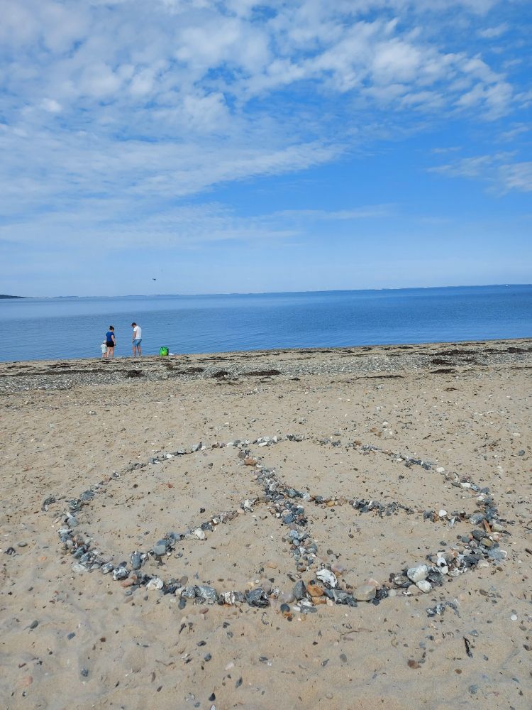 Peace sign made of stones on a beach with the sea in the background.