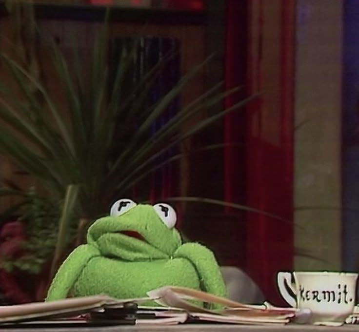 Kermit the frog sitting at a desk with papers 