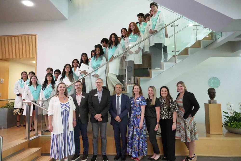 Students standing on a staircase with faculty members standing on the floor below.