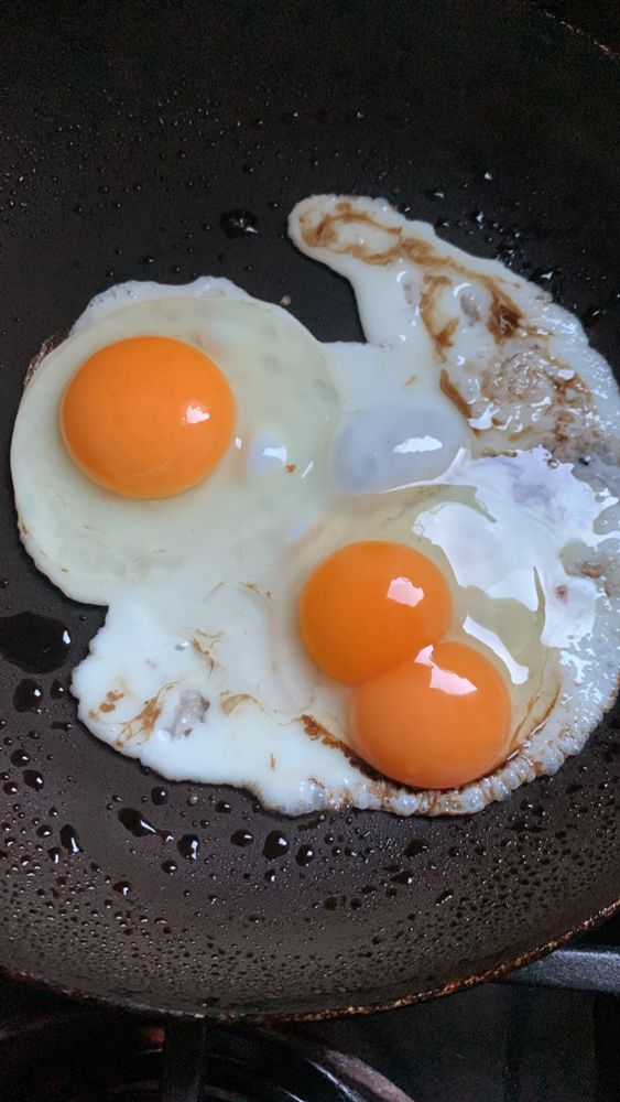 2 eggs frying in a pan, one is a double yolk. 