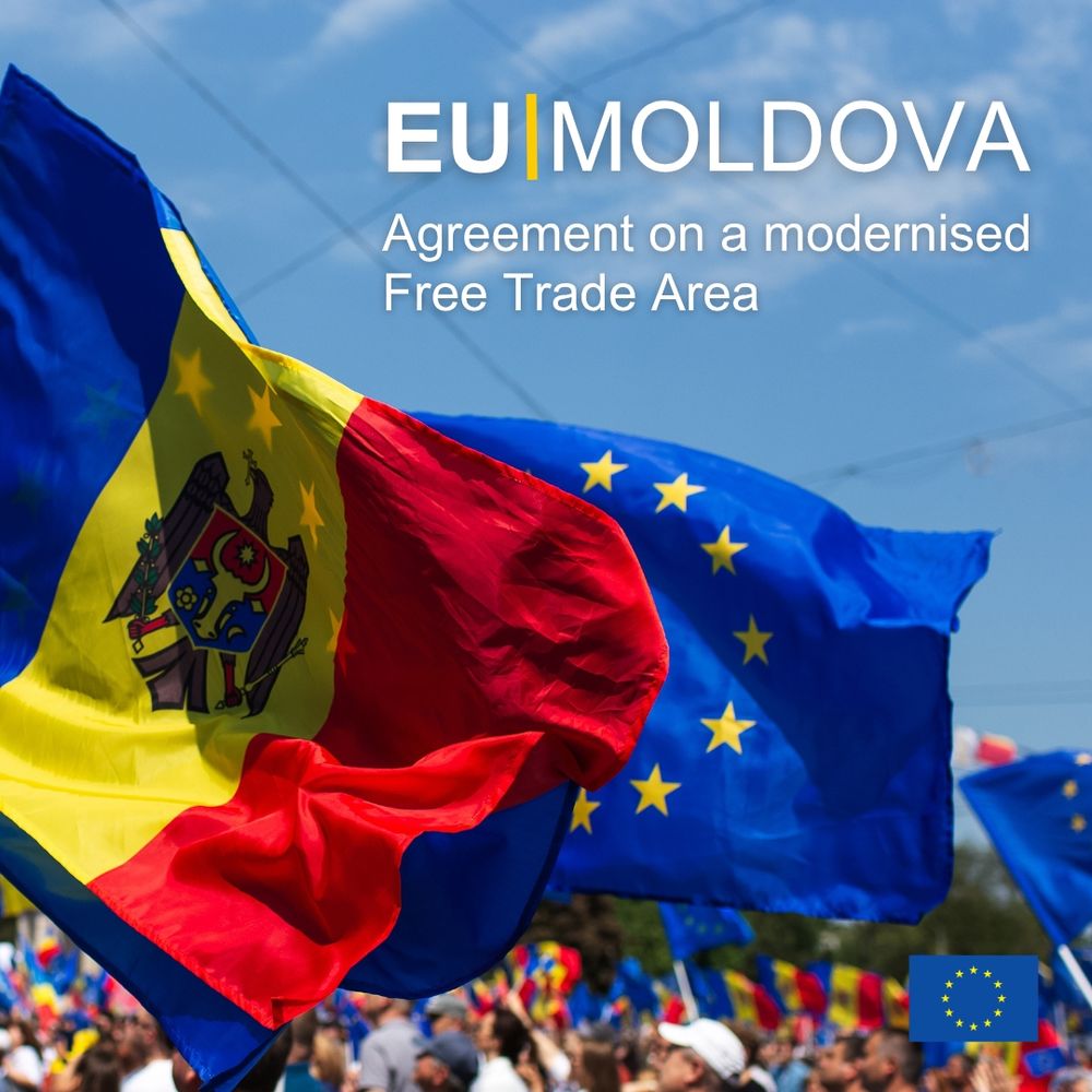 A bright blue sky background, featuring large Moldovan and European Union flags waving over a blurry crowd. The text 'EU Moldova Agreement on a modernised Free Trade Area' is prominently displayed in white. A smaller EU flag logo is in the bottom right corner. 
