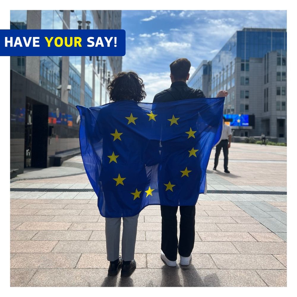 Two people hold an EU flag, standing outside a modern building, encouraging participation in a discussion.