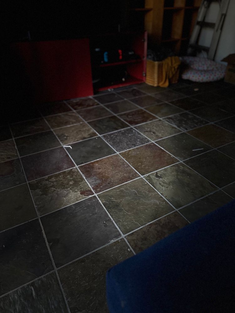 A slate floor. It’s lit only in a globular oval in the middle of the frame, while the rest is in shadow. 