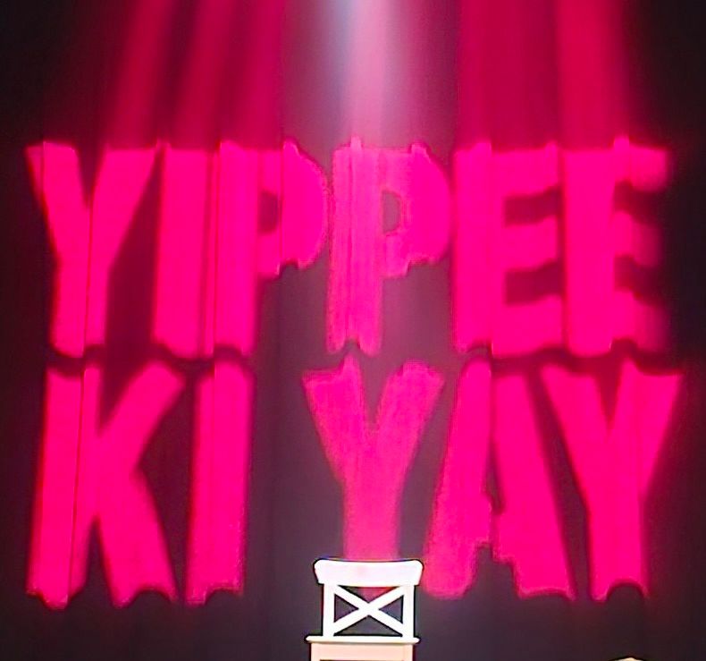 Red text saying “Yippee Ki Yay” on the background of a stage.