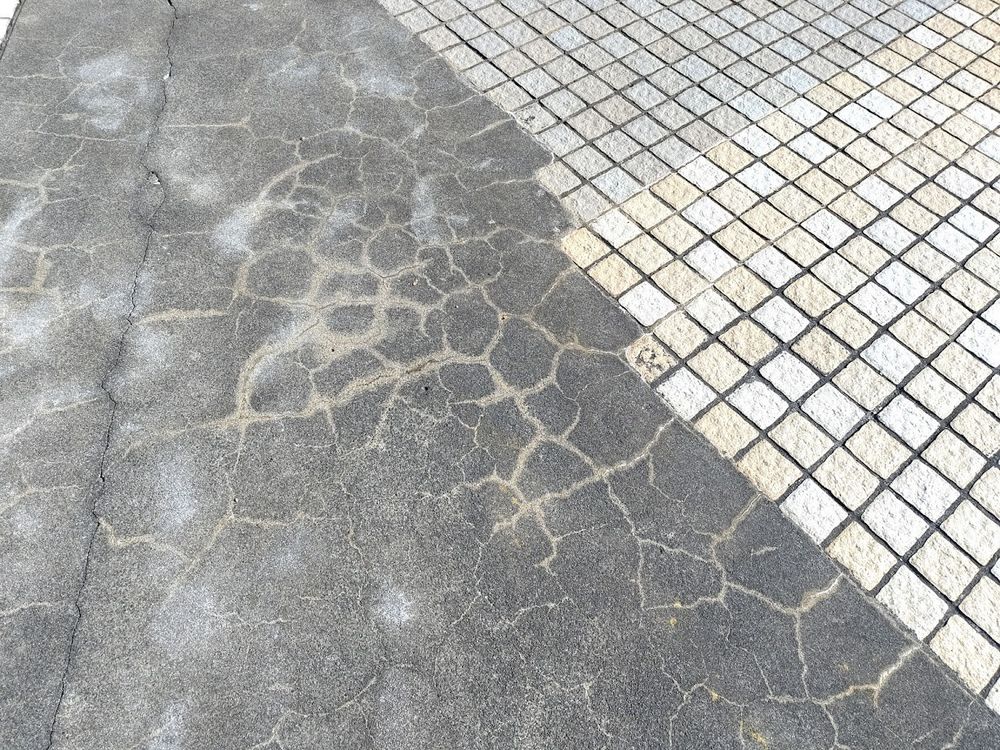 Cracked asphalt/tarmac surface next to grey & beige toned block tiles in Aoiumi Park, texture reference
