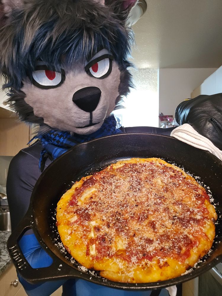 wolf bravely posing with a hot pizza in a cast iron pan